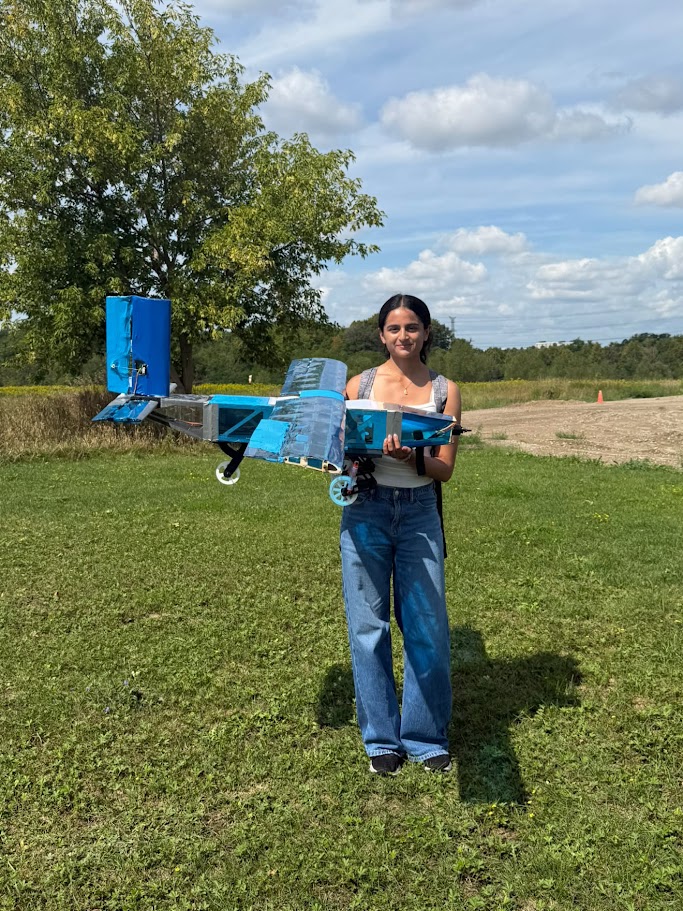 Yashvi Shah holding a blue RC aircraft in a field