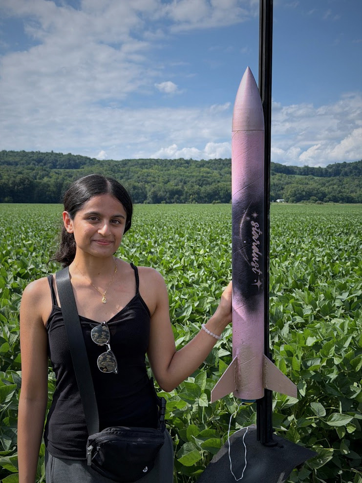 Yashvi Shah holding a scratchbuilt high-power rocket in a field